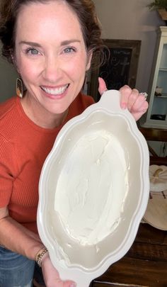 a woman holding up a large white plate with frosting on it's side