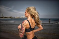 a woman running on the beach with tattoos on her arm and back, in a sports bra top