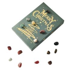 a green christmas card surrounded by small rocks and stones on a white background with the words merry christmas written in gold