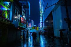 people walking down the street at night with umbrellas