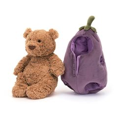 a brown teddy bear sitting next to a small purple backpack on a white background,