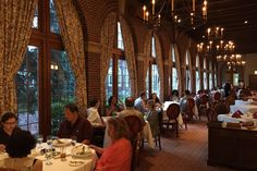 people sitting at tables in a restaurant with large windows and chandeliers hanging from the ceiling