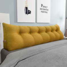 a bed with a yellow tufted headboard and two pictures on the wall above it