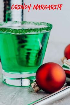 a green glass filled with liquid next to two red ornaments