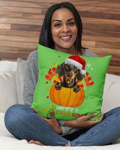 a woman sitting on a bed holding a pillow with a dachshund wearing a santa hat