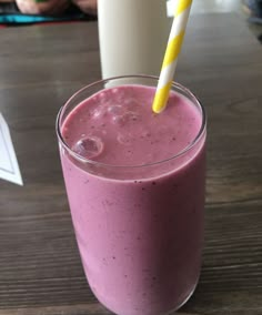 a pink smoothie in a glass with a yellow and white striped straw sitting on a table