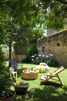 an outdoor area with lawn chairs, tables and potted plants on the grass in front of a stone building