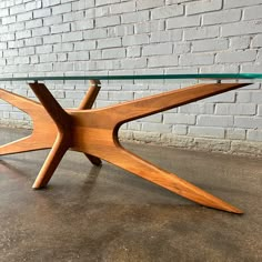 a wooden table with glass top sitting in front of a brick wall on concrete flooring