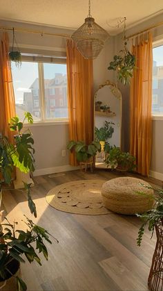 a living room filled with lots of plants next to two large windows covered in orange drapes