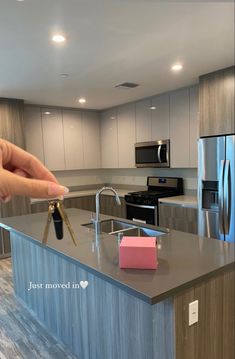 a hand holding a house key in front of a kitchen island