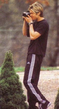 a man taking a photo with a camera in front of some bushes and trees on the ground