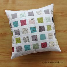 a white pillow with colorful patchwork on it sitting on top of a wooden table