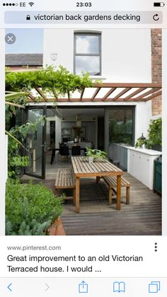 a wooden table sitting on top of a wooden deck next to a white building with lots of windows