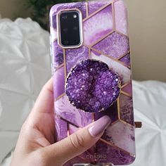 a woman holding up her phone case with purple and pink marble design on it's back