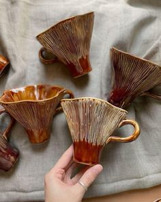 someone is holding their hand out to five coffee mugs that are shaped like leaves