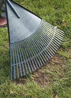 a person standing in the grass with a large metal rake