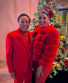 a man and woman dressed in red standing next to a christmas tree