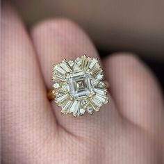 a close up of a person's hand holding a ring with an emerald and diamond center