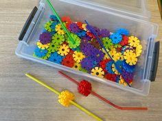 a plastic container filled with lots of colorful gears and straws on top of a wooden table