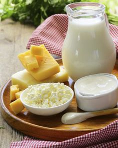 a wooden plate topped with cheese, milk and other foods on top of a table