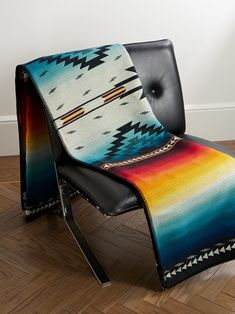 a multicolored blanket sitting on top of a black leather chair in front of a white wall