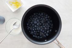 blueberries are being cooked in a saucepan with spoons on the table next to it