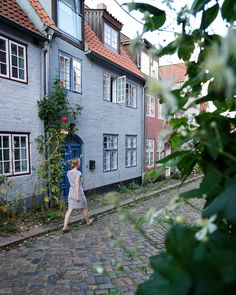 a woman walking down a cobblestone street in front of some old buildings with blue doors