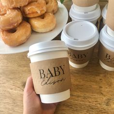 a person holding up a cup of coffee next to doughnuts