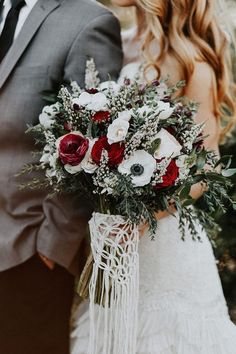 a bride and groom standing next to each other in front of a christmas tree with red and white flowers