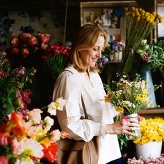 a woman standing in front of a flower shop holding a cup with flowers on it