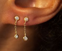 a close up of a person's ear wearing gold and diamond earrings with chain links