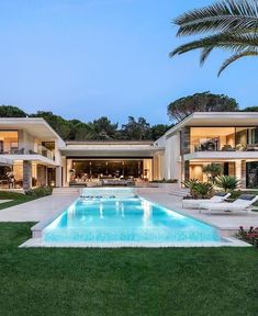 an outdoor swimming pool with lounge chairs and palm trees in front of a large house