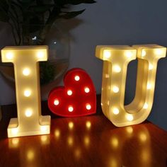 lighted letters spelling out the word love on a wooden table next to a potted plant