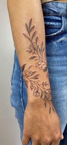 a woman's arm with a tattoo on it that has leaves and flowers on it