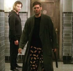 two men standing in a bathroom with one holding a knife