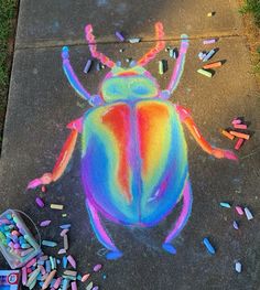 a colorful bug drawn on the sidewalk next to crayons and chalk sticks in front of it