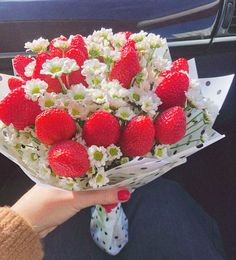 a person holding a bouquet of strawberries and daisies in their hand while sitting in the back seat of a car