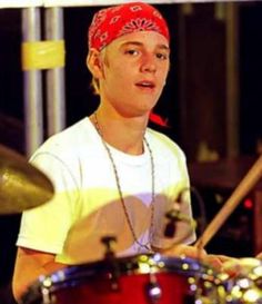 a young man is playing the drums in front of his drum set and wearing a bandana