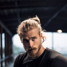 a man with long hair and a beard wearing a black t - shirt looking at the camera