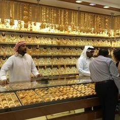 people are looking at gold necklaces on display in a store with men standing behind the counter