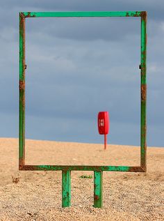 a square shaped object in the sand with a blue sky behind it and a red sign