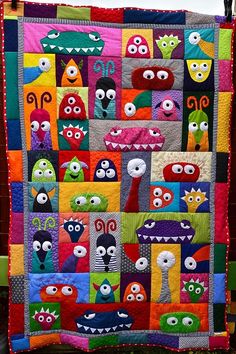 a quilt made to look like monsters with eyes and mouths on the front, hanging from a clothes line