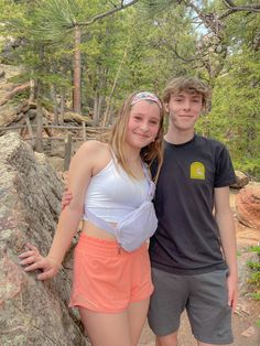 two young people standing next to each other on a rocky surface with trees in the background