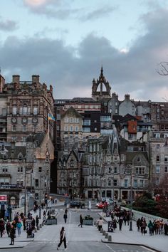 many people are walking around in front of some old buildings on a cloudy day at dusk