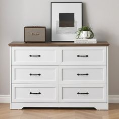 a white dresser with black handles and drawers in front of a framed photograph on the wall