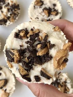 a hand holding a chocolate chip cookie with white frosting and chopped walnuts on top