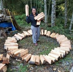 a woman standing in the middle of a circle made out of firewood logs and holding two large pieces of wood