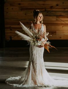 a woman in a white dress holding a bouquet and standing next to a wooden wall