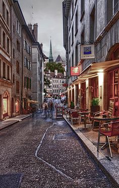 an empty street with tables and chairs on the sidewalk in front of some old buildings