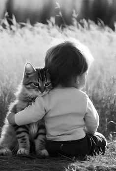 a little boy sitting in the grass hugging a cat